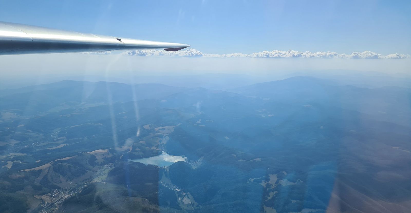 Zalesnené hory s vodnou nádržou pod krídlom vetroňa
